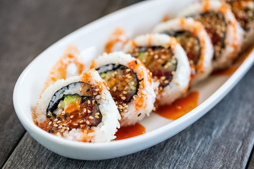Sushi rolls with sesame seeds and orange sauce on a white platter.