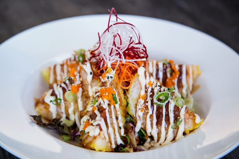 Triangular sushi pieces topped with white sauce, orange roe, and shredded vegetables on a white plate.