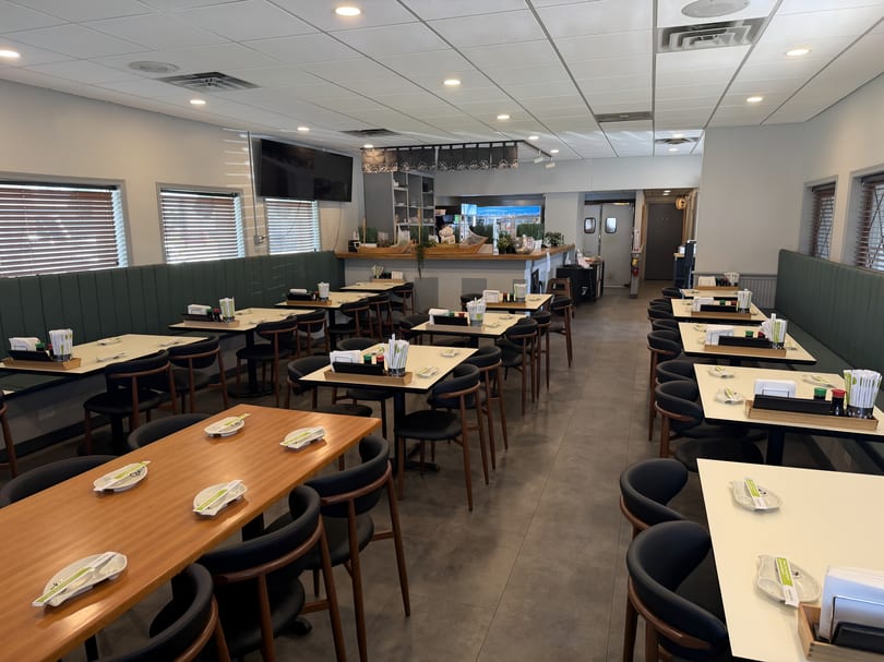 A brightly lit, empty restaurant dining room with tables, chairs, and booth seating.