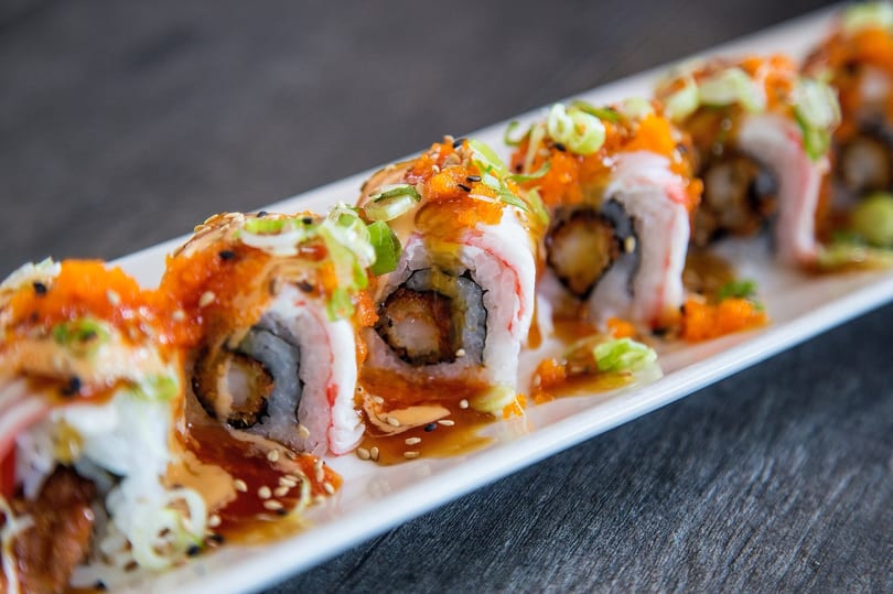 Sushi rolls with shrimp tempura, crab, roe, scallions, and sauce on a white plate.