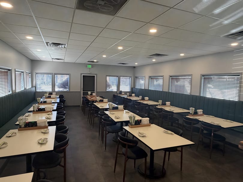 Empty restaurant dining room with rows of tables, chairs, and booths, set with chopsticks and dishes.