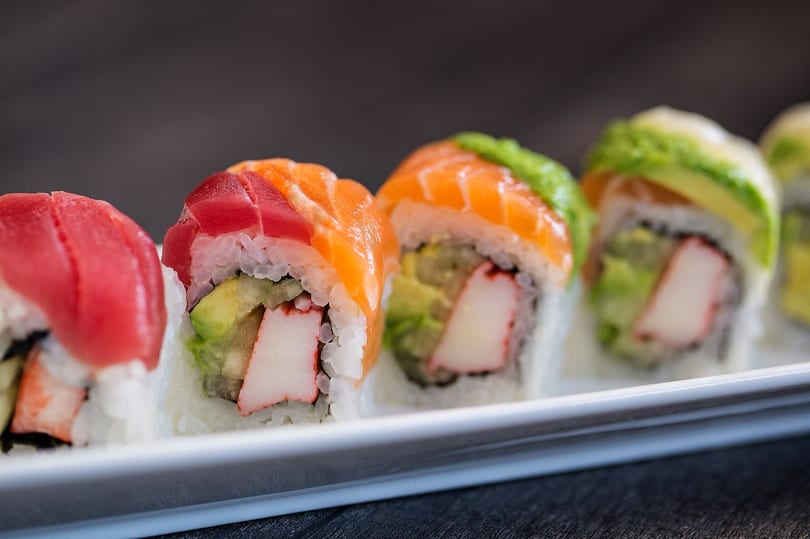 Colorful sushi rolls with tuna, salmon, avocado, and crab meat on a white rectangular plate.
